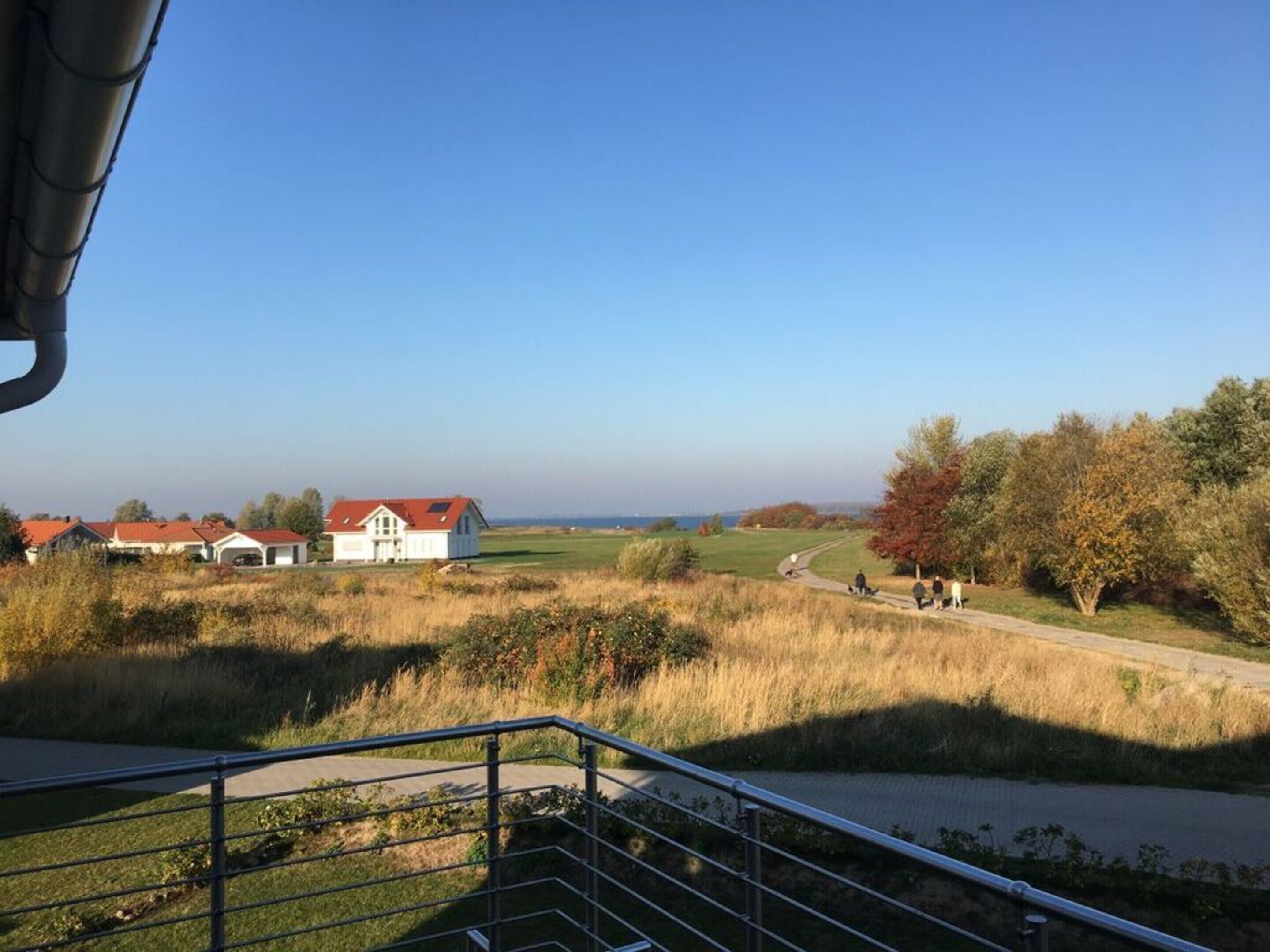 Et landligt landskab med et hvidt hus, en sti og et metalgelænder.