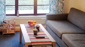 A living room with a sofa, a coffee table with a bowl of fruit and two cups, a radiator, and a window with curtains. - 8 Person Holiday Home in Hogklint-by Traum (Visby)