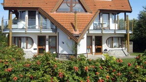 Uma casa de dois andares com telhado triangular, varandas e um jardim com frutas vermelhas.