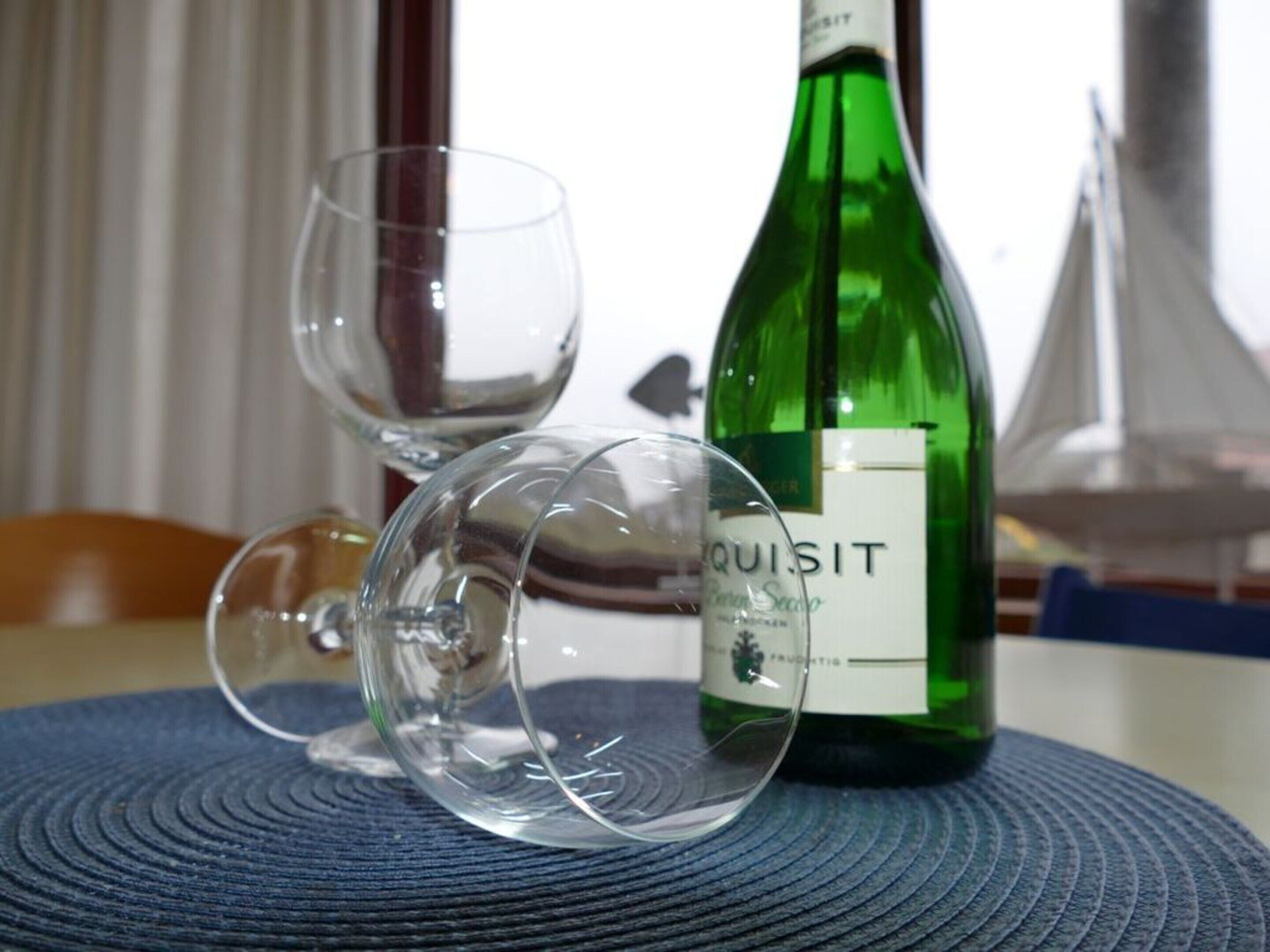 A green wine bottle labeled 'QUIJIT' on a table with two empty wine glasses.