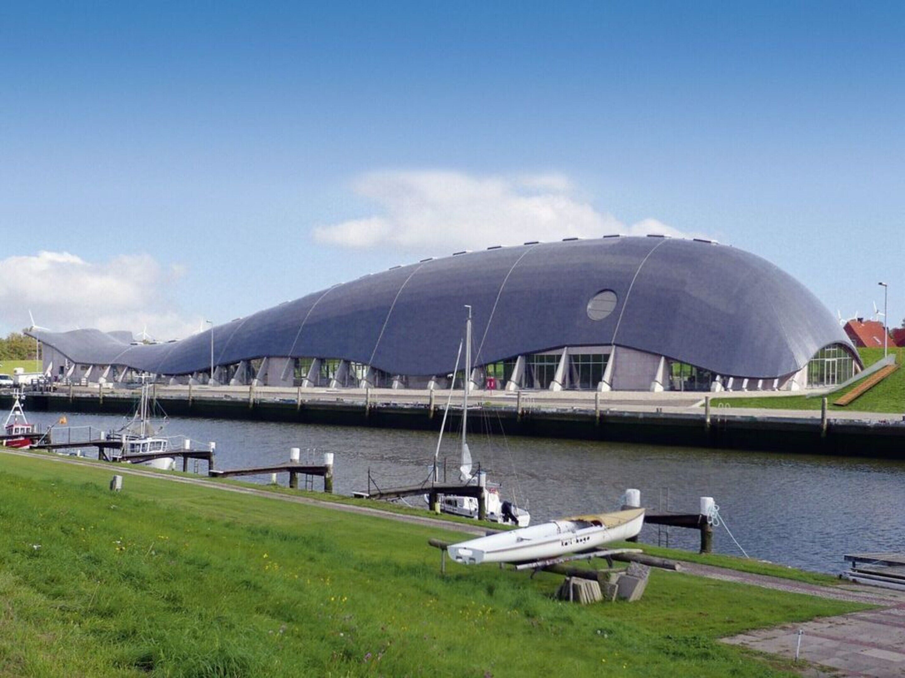 A modern architectural building with a unique curved roof, situated next to a body of water with boats docked.