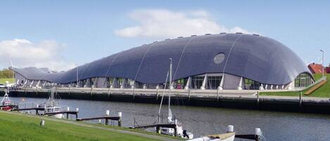 A modern architectural building with a unique curved roof, situated next to a body of water with boats docked.