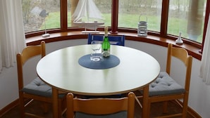 Uma mesa de jantar redonda com quatro cadeiras, uma garrafa de vinho e um copo sobre um jogo americano.