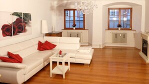 A spacious living room with a white sofa, red cushions, a glass coffee table, and a chandelier. - Lake Constance Hearts (Meersburg)