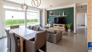 A modern living room with a dining area, a sofa set, a TV, and a green accent wall. - Oud Klooster 0001 Apartment in De Haan (De Haan)