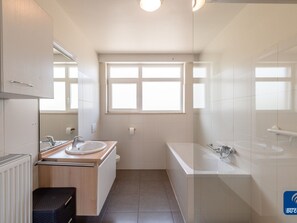 A modern bathroom with two sinks, a bathtub, and a window providing natural light. - Oud Klooster 0001 Apartment in De Haan (De Haan)