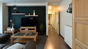 A modern living room with a flat-screen TV, wooden furniture, and a hallway leading to another room. - Oud Klooster 0001 Apartment in De Haan (De Haan)