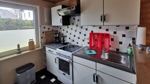 A compact kitchen with white cabinets, a black stove, and a window with blinds. - Kubis Modern Retreat (Wiek)