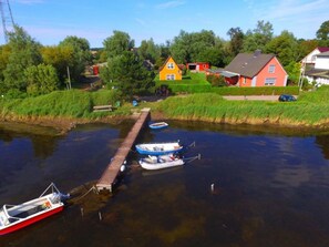 Un muelle a la orilla del río con barcos, un embarcadero de madera y casas al fondo.