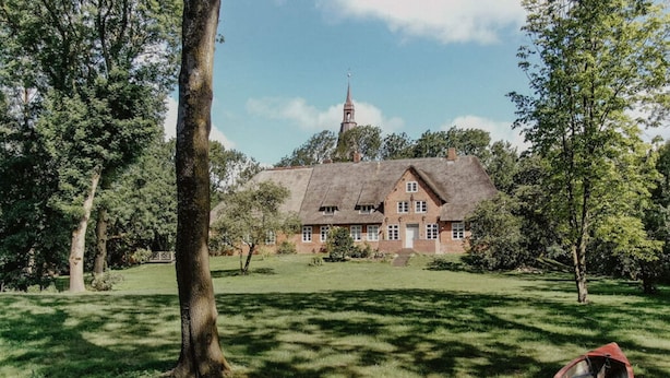 Ett traditionellt hus med ett halmtak, omgivet av en frodig grön gräsmatta och träd.