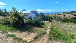 Propiedad costera con un edificio blanco, un camino de tierra y abundante vegetación.