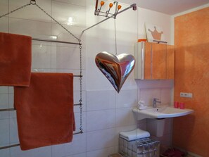 Un bagno con un lavandino bianco, pareti arancioni e uno specchio a forma di cuore.