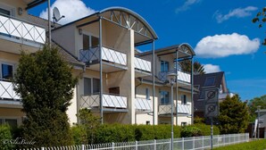A multi-story residential building with balconies, a white fence, and a clear blue sky. - Holiday Apartment New Love (Zingst)