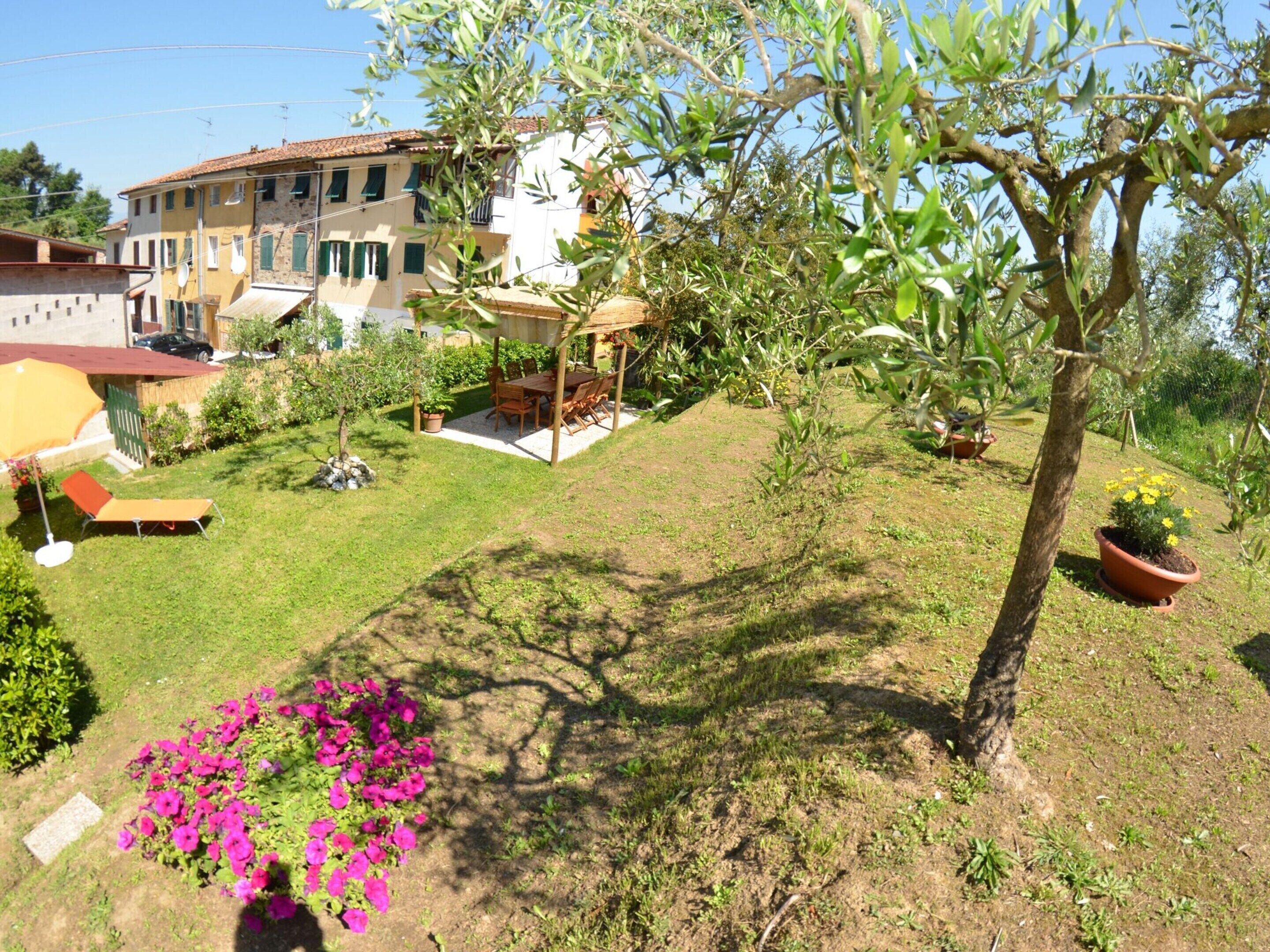 Un quartiere residenziale con una casa, un patio con tavolo e sedie, e un piccolo giardino con fiori e un albero.