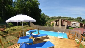 A wooden deck with a pool, blue lounge chairs, and a white umbrella. - Holiday Home in Lucca With Pool & Garden (Pescaglia)