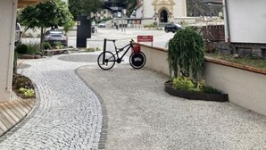 En brostensbelagt sti der fører hen til en kirke med et højt spir, omgivet af bygninger og et bjerg i baggrunden.