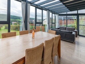 A spacious room with a large table and wicker chairs, a grey sofa, and a glass ceiling offering a view of the countryside. - Cozy Holiday Home in Malmedy With a Beautiful View (Malmedy)