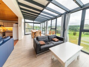 A modern living room with a glass ceiling, a black leather sofa, a white coffee table, and a dining area with wooden furniture. - Cozy Holiday Home in Malmedy With a Beautiful View (Malmedy)