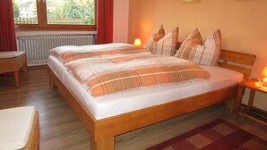 A bedroom with a wooden bed, plaid bedding, a window with curtains, a bedside table with a lamp, and a view of greenery outside. - Holiday Apartment Anita Wald (Bad Muenstereifel)