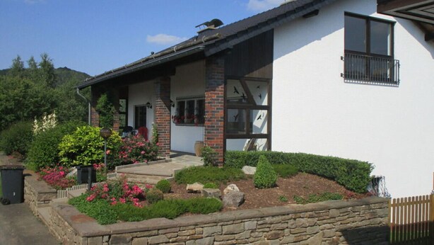 A modern house with a brick facade, a covered porch, and a well-maintained garden with flowers and shrubs. - Holiday Apartment Anita Wald (Bad Muenstereifel)