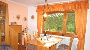 A dining area with a wooden table, four chairs, a radio, and a window with curtains. - Holiday Apartment Anita Wald (Bad Muenstereifel)