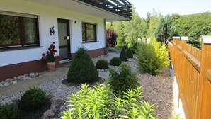 A two-story house with a balcony, surrounded by a well-maintained garden with various shrubs and a wooden fence. - Holiday Apartment Anita Wald (Bad Muenstereifel)