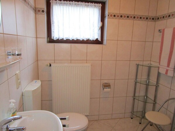 Un baño pequeño con inodoro, lavamanos y ventana con cortina blanca.