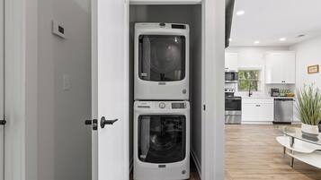 A laundry room with two stacked front-loading washing machines, a microwave, and a dishwasher in a modern kitchen.