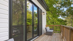 Une terrasse dotée d’une porte-fenêtre coulissante donnant sur un espace patio, d’un canapé en osier et d’une rambarde en bois.