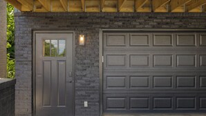 Une porte de garage adossée à un mur en briques, avec une porte dotée d’une fenêtre.