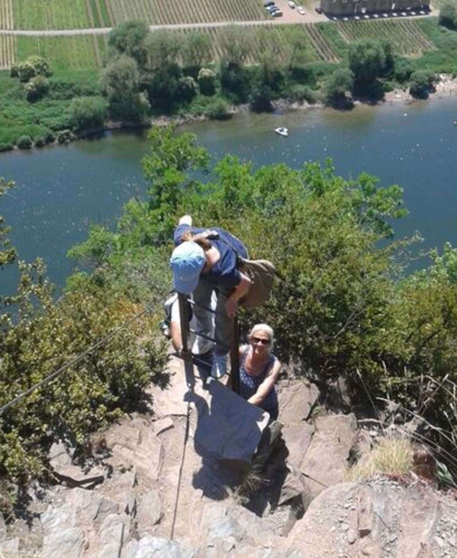A group of people on a rocky ledge with a river and fields in the background.