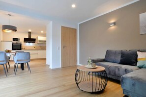A modern living room with a grey sofa, a round coffee table, and a dining area with chairs and a small table. - Lovely Apartment in Hambuch (Hambuch)