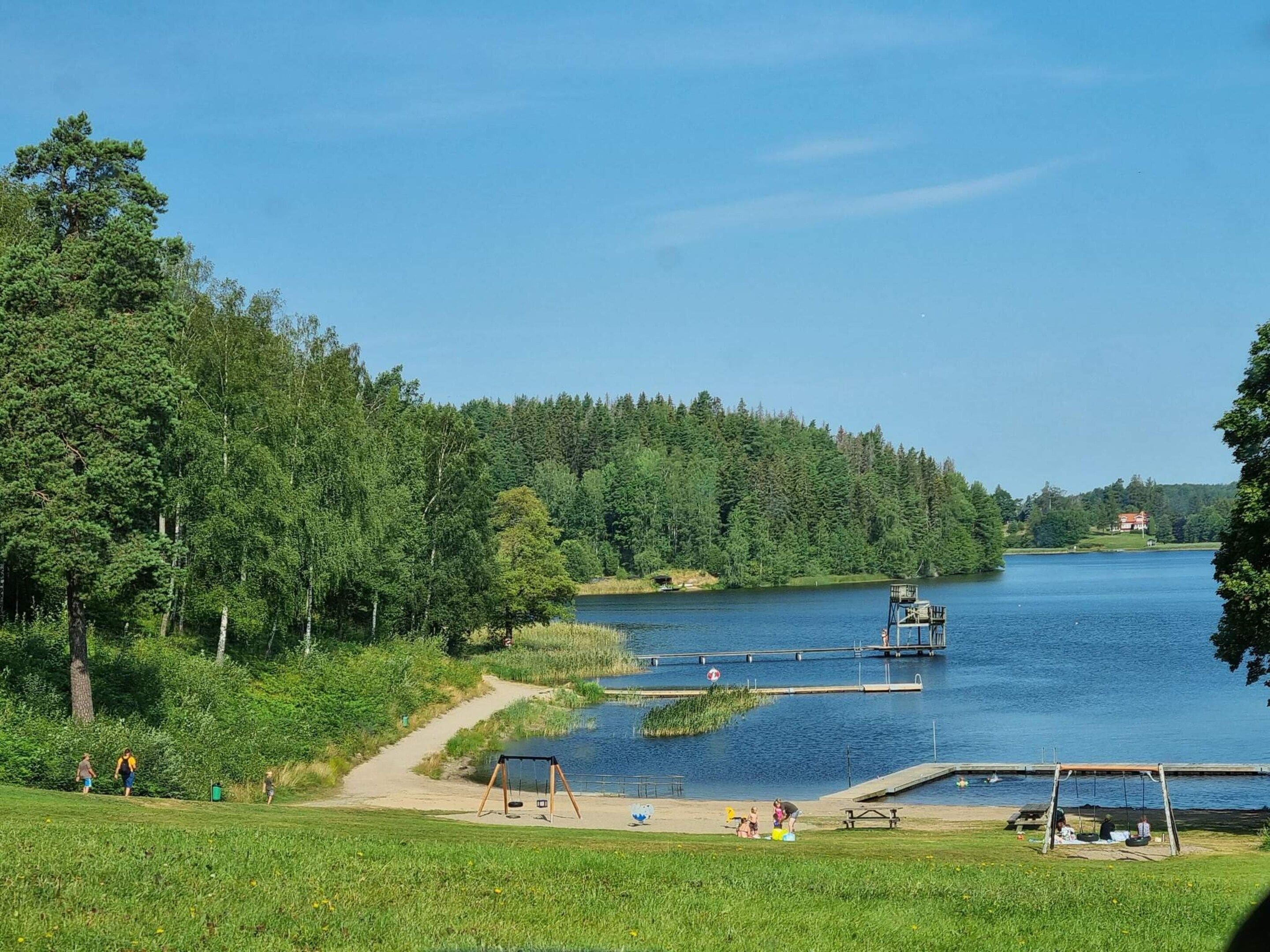 A lakeside park with a swing set, picnic tables, and a dock extending into the water.
