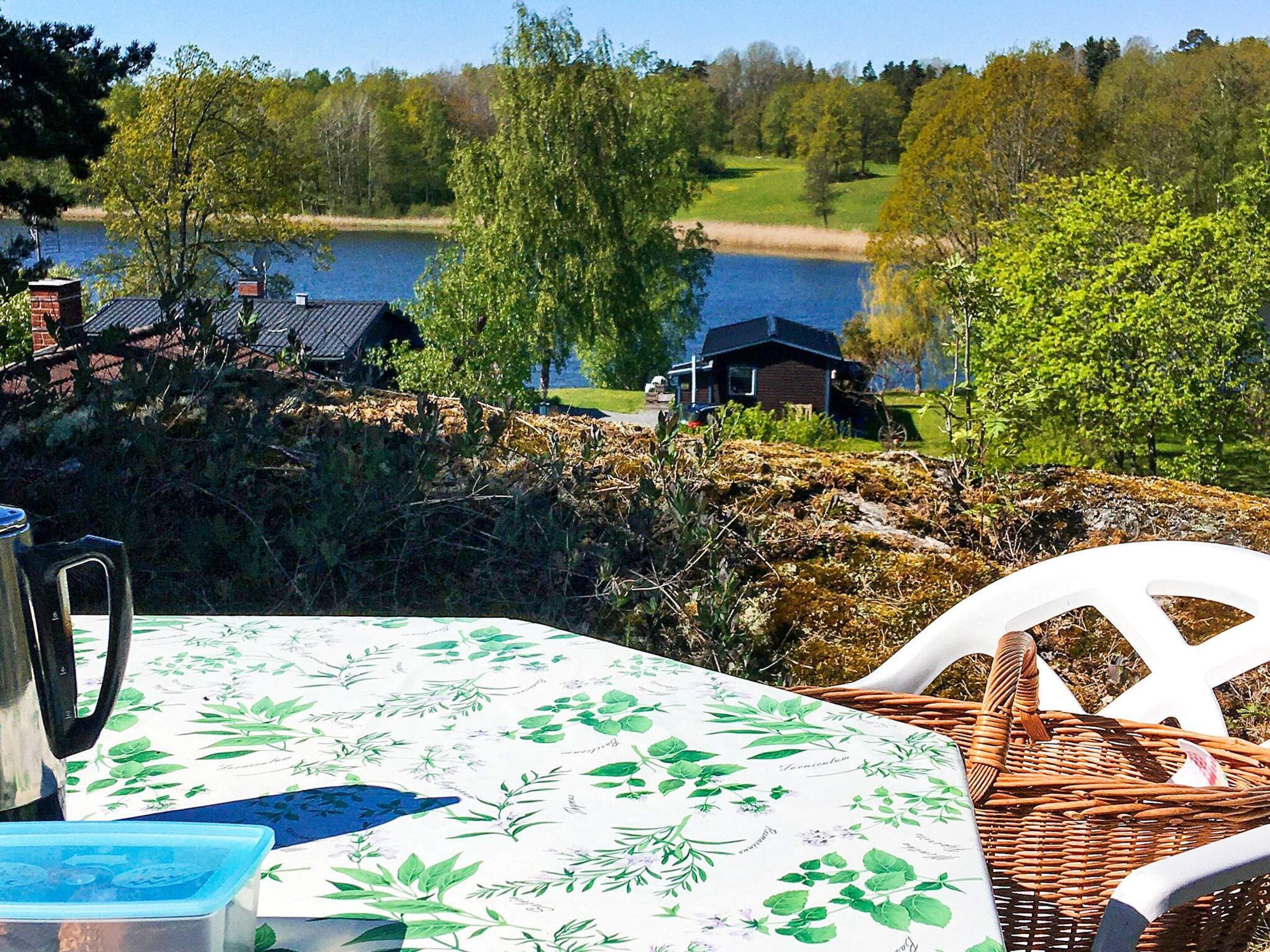 Une table recouverte d’une nappe à motifs botaniques, une chaise en osier et une bouilloire en métal.