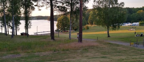 A lakeside park with picnic areas, a small building, and tall trees.