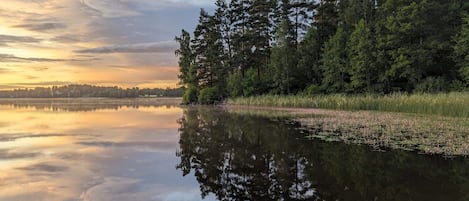 A calm lake with dense forest on one side and a clear sky.