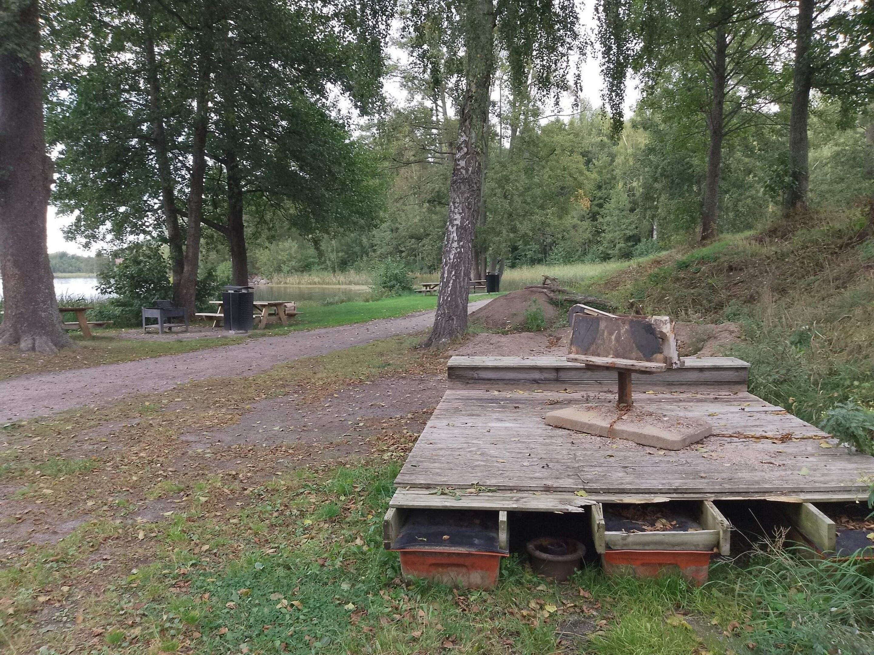 A park with picnic tables, a dirt path, and a wooden platform with benches.