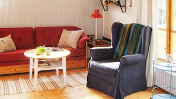 A living room with a red sofa, a round coffee table, a blue armchair, a patterned rug, and a window with a view of trees.