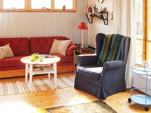 A living room with a red sofa, a round coffee table, a blue armchair, a patterned rug, and a window with a view of trees. - 4 Star Holiday Home in Malmkoping (Malmkoping)