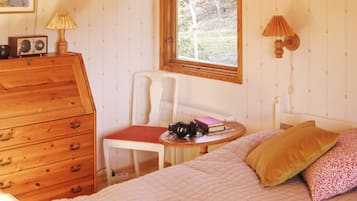 Une chambre à coucher avec un lit, une commode en bois, une chaise, une table avec une lampe et une fenêtre.