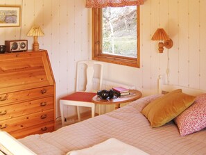 A bedroom with a bed, a wooden dresser, a chair, a table with a lamp, and a window. - 4 Star Holiday Home in Malmkoping (Malmkoping)