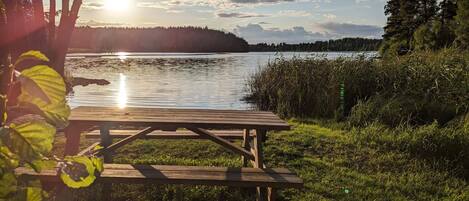 A wooden picnic table by a lake with a clear sky and distant trees.