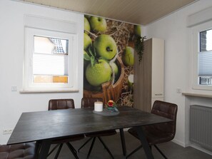 A dining area with a dark wooden table, four brown leather chairs, and a wall mural of green apples. - Elas Place Modern Retreat (Thür)