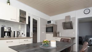 A modern kitchen with white cabinets, a coffee machine, and a microwave. There is a dining table with a vase of flowers and a candle. - Elas Place Modern Retreat (Thür)