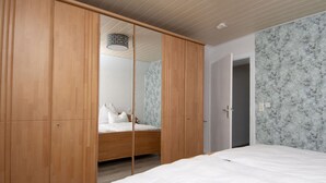 A bedroom with a wooden wardrobe, a bed with white bedding, and a marble-patterned wall. - Elas Place Modern Retreat (Thür)