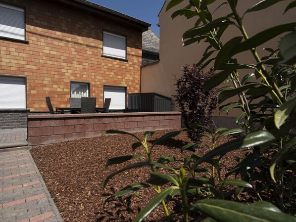 A brick building with a flat roof, a patio with chairs, and a small garden area with mulch and plants. - Elas Place Modern Retreat (Thür)