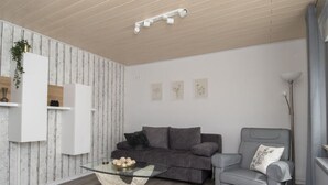 A modern living room with a grey sofa, a grey armchair, a glass coffee table, and a white wall with wooden paneling. - Elas Place Modern Retreat (Thür)