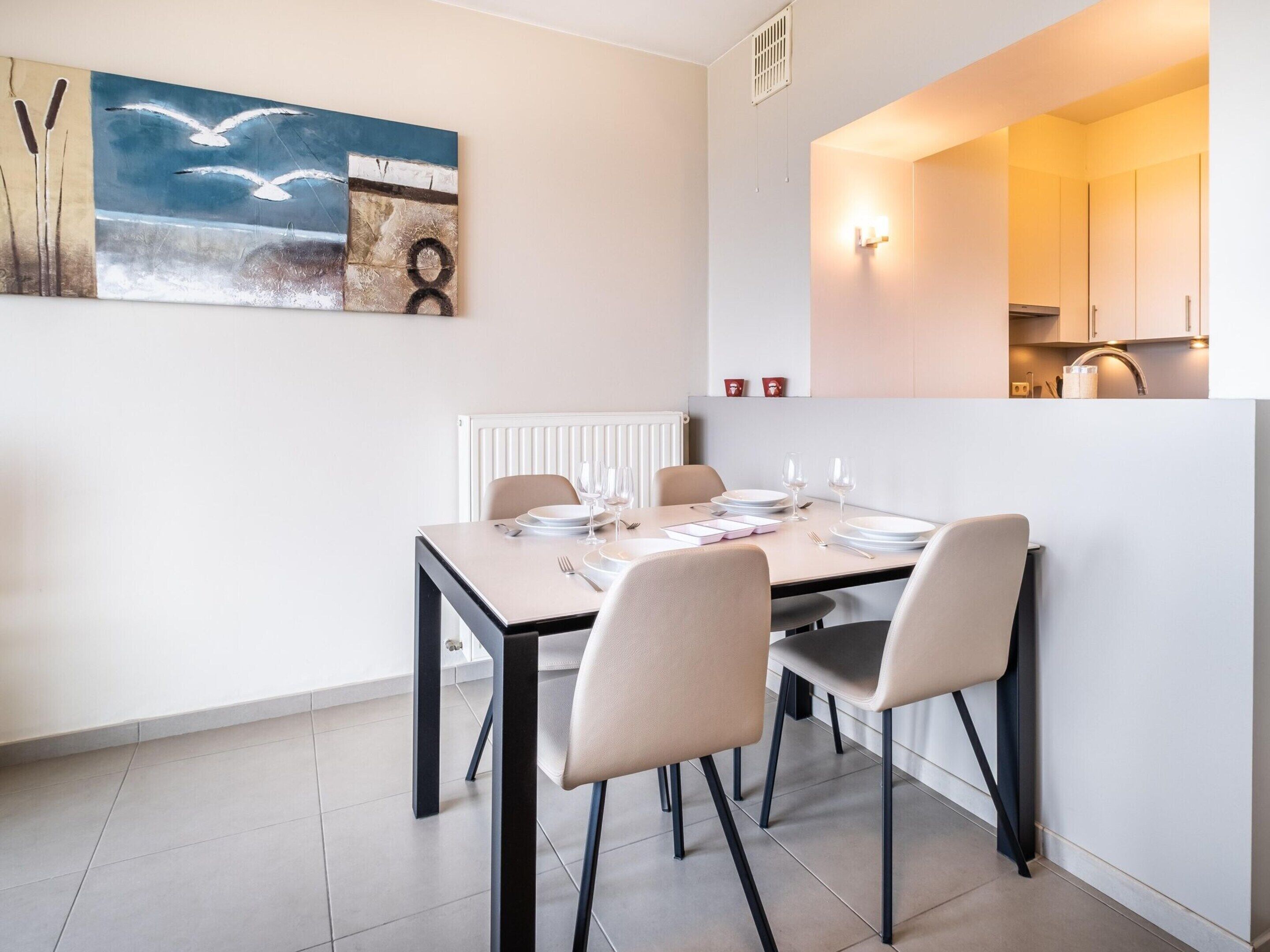 A dining area with a table set for four, chairs, a radiator, and a painting on the wall.