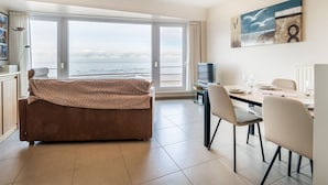 Ein modernes Zimmer mit großem Fenster, einer Couch, einem Esstisch mit Stühlen, einem Fernseher und einem Bild an der Wand.