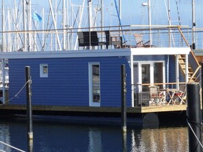 A blue docked boat with a covered deck area and a small open doorway. - Lasse Comfortable Holiday Residence (Heiligenhafen)